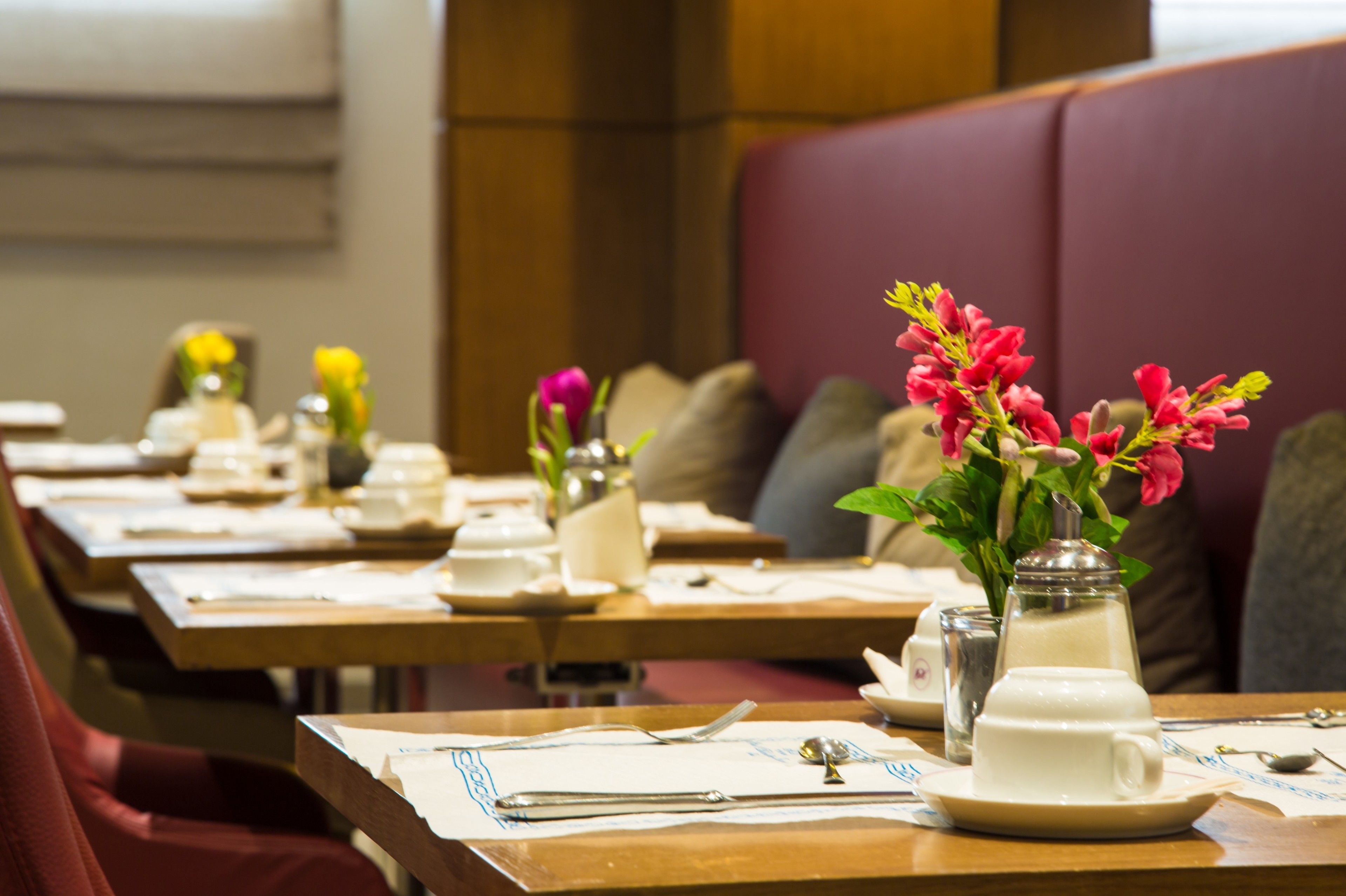 A dining area with tables set for service, each with a vase of flowers, a sugar bowl, and a creamer.
