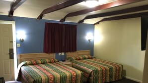 A room with two beds, a wooden headboard, a red curtain, and a small table. - Blarney Inn (Shamrock)