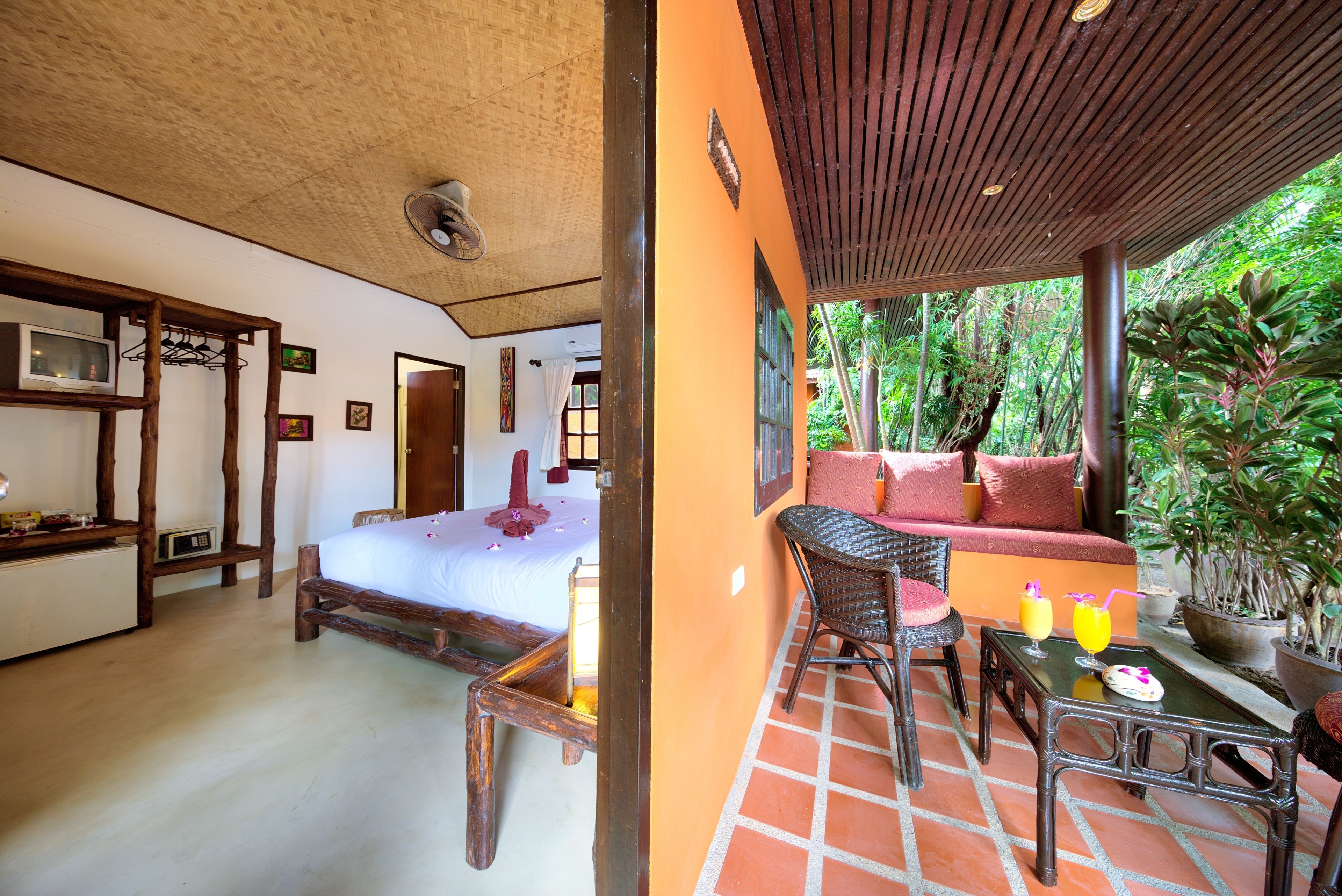 A room with a bed, a wooden chair, a table with drinks, and a sofa with cushions.