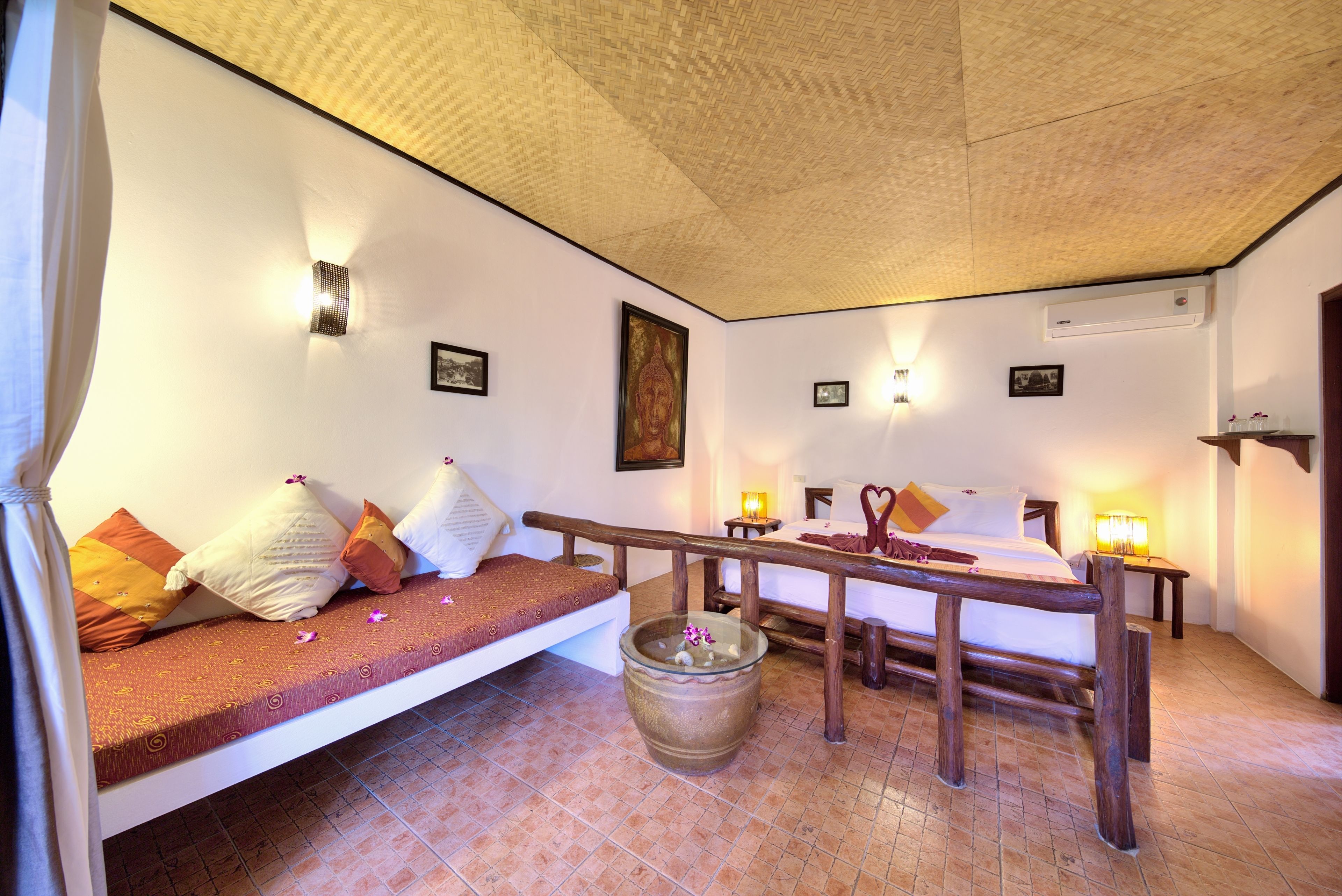 A room with a bed, a small table, a wooden bench, and a decorative pot.