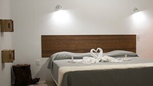 A neatly made bed with a wooden headboard, a fluffy white throw, and a heart-shaped towel arrangement on the bed. - Hotel Karenina (Oaxaca)