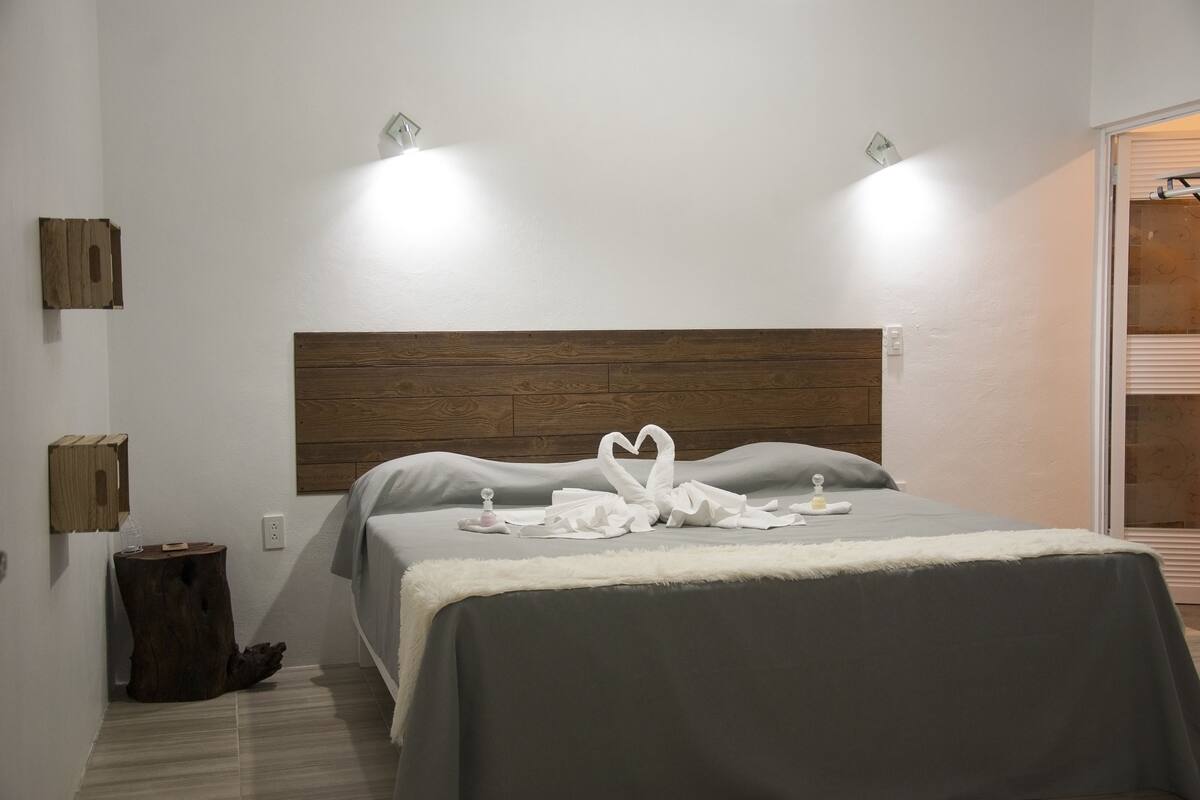 A neatly made bed with a wooden headboard, two wall-mounted lights, and a small wooden stool.