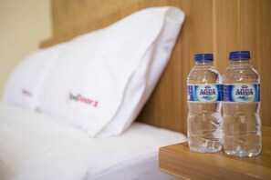 A bed with white bedding and two bottles of Aquafina water on a wooden nightstand. - RedDoorz Plus @ Guntur Raya Setiabudi (Jakarta)