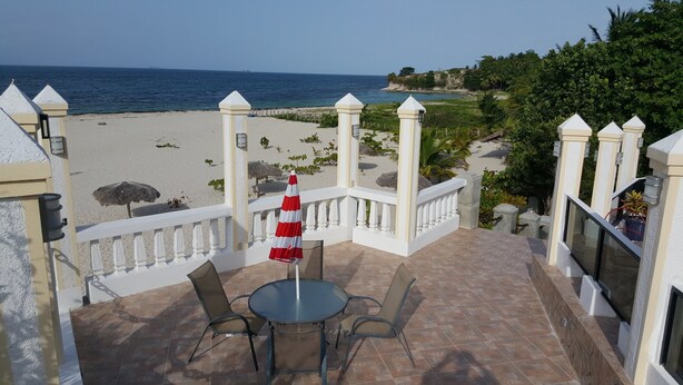 Uma varanda com mesa e cadeiras, com vista para uma praia e uma visão clara do oceano e terra ao longe.