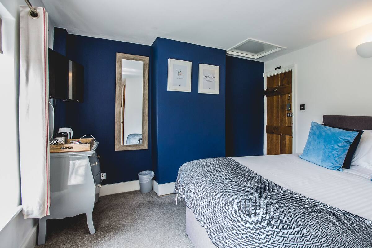 Quarto com cama, mesa de cabeceira, espelho e porta.