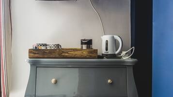 A modern room with a flat-screen TV mounted on the wall, a wooden tray with a coffee maker and mug, and a grey dresser with gold knobs.