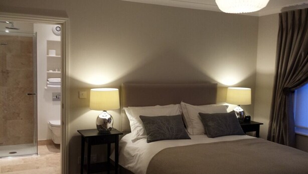 Une chambre d’hôtel avec un grand lit, deux tables de chevet avec des lampes, un espace douche et une salle de bain.