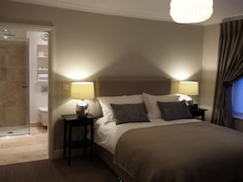 Habitación de hotel con una cama grande, dos mesitas de noche con lámparas, zona de ducha y baño.