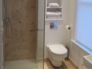 Bathroom features a glass-enclosed shower, toilet, and storage shelf.