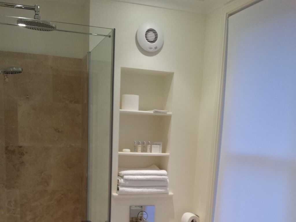 A bathroom with a glass shower enclosure, a toilet, and a shelf with toiletries.