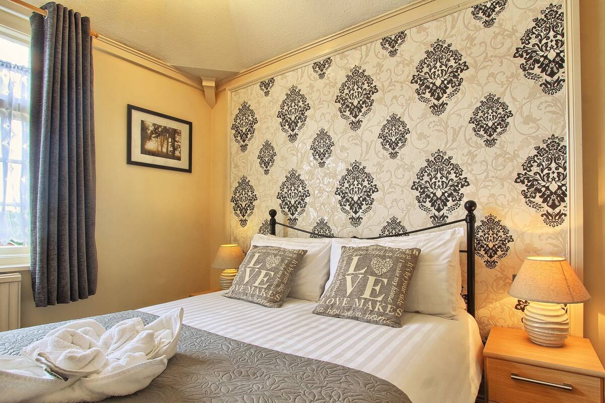 Een netjes opgemaakt bed met decoratieve kussens, een bedlampje en een bekleed hoofdeinde.