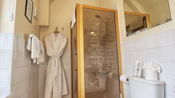 Un baño con mampara de vidrio, inodoro blanco y perchero con batas.