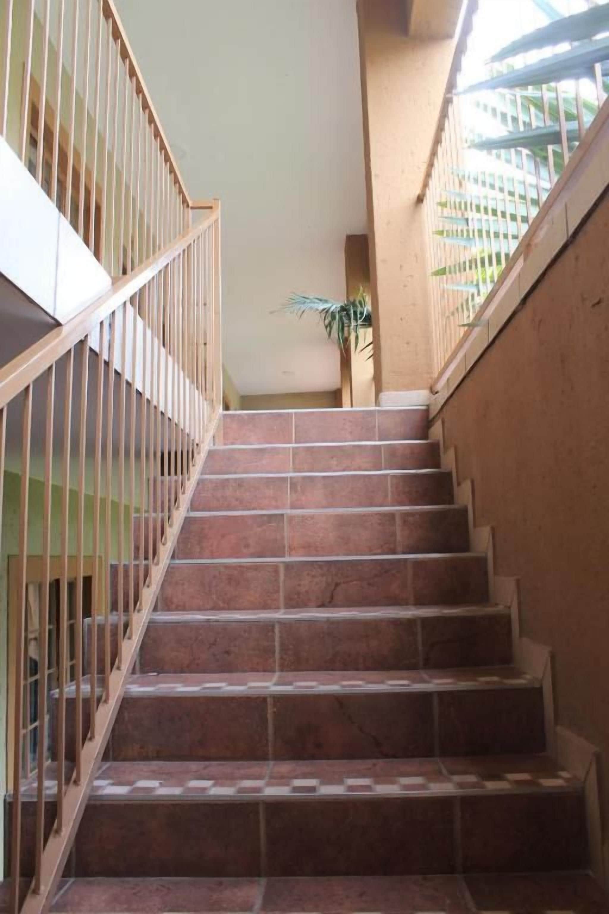 Un escalier avec des rampes en bois et des marches recouvertes de carreaux rouges, menant à un palier.
