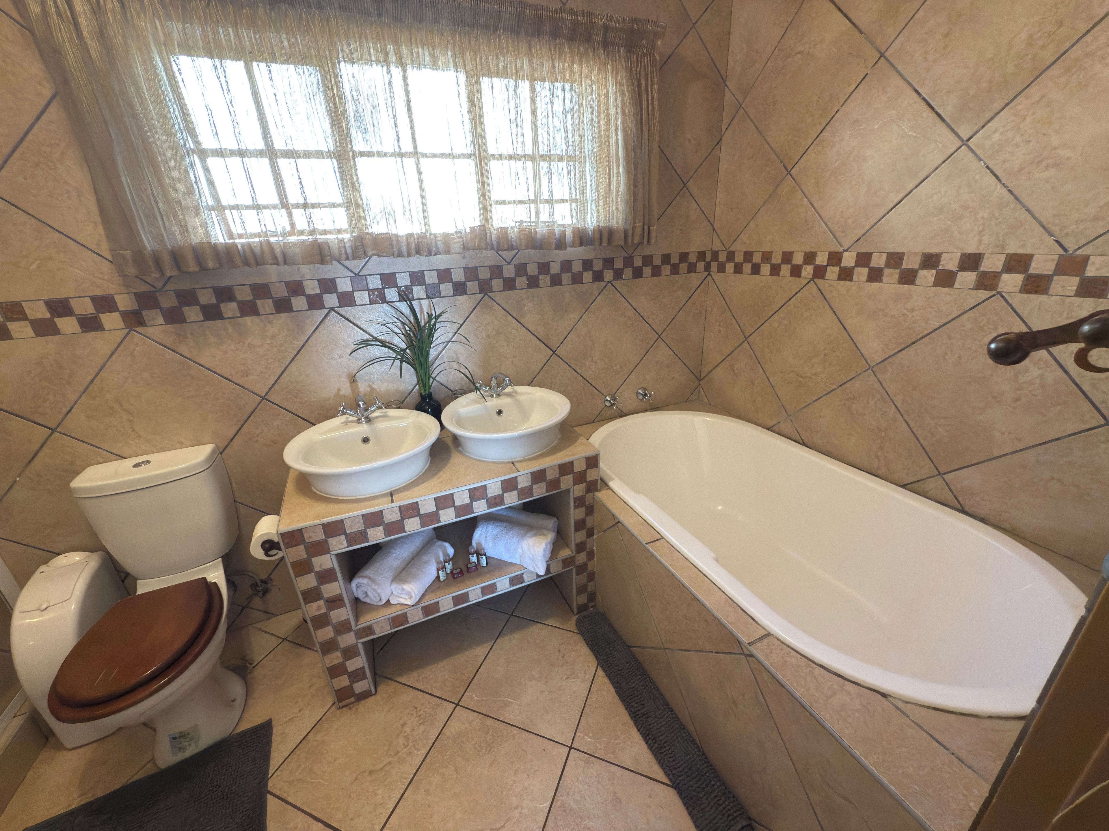 A bathroom with a toilet, two sinks, a bathtub, and a window with curtains.