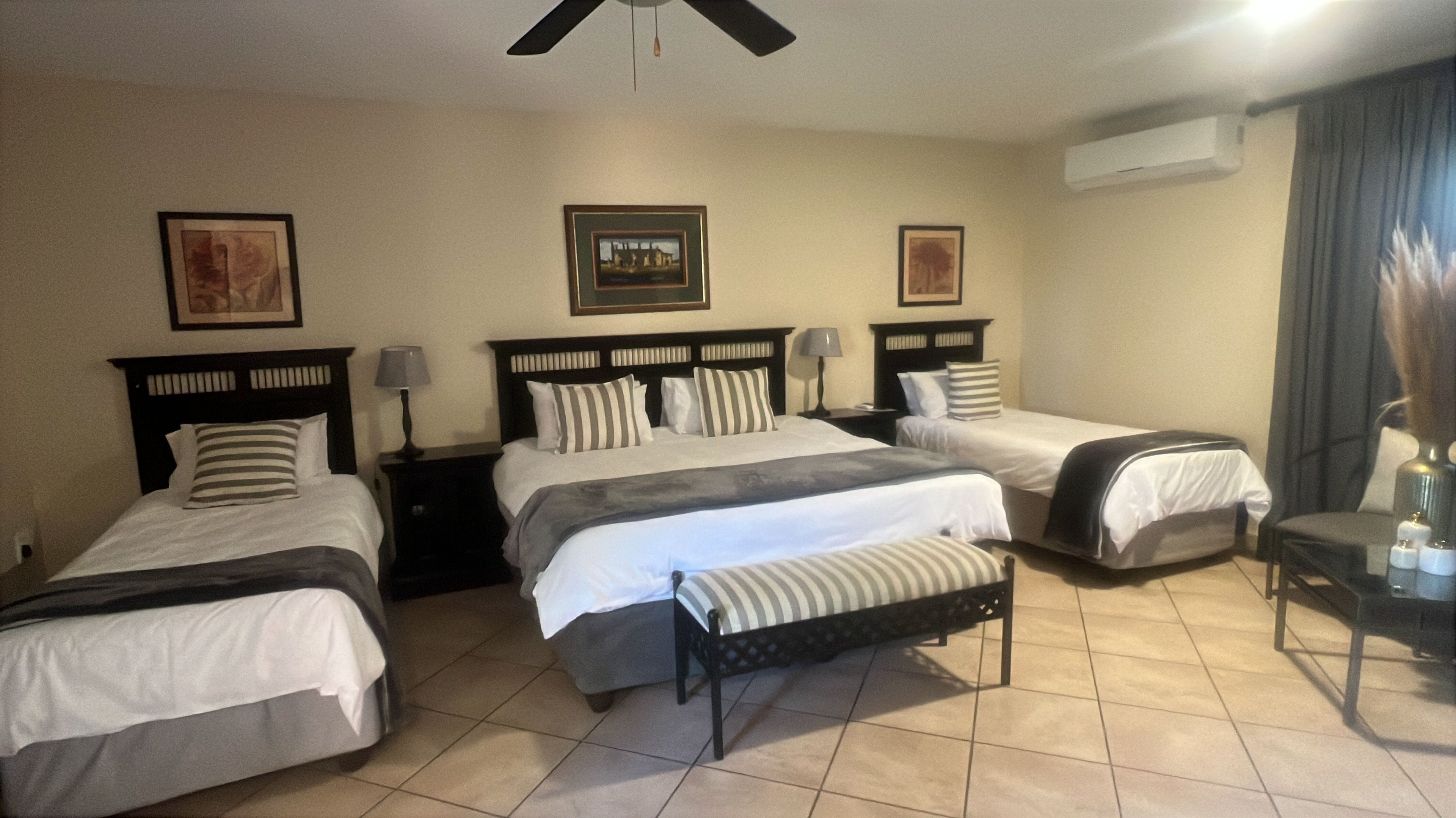 A hotel room with three beds, a ceiling fan, and a nightstand with a lamp.