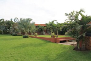 A well-maintained garden with palm trees and a red building in the background. - Batter Boys Boutique Hotel (Pretoria)
