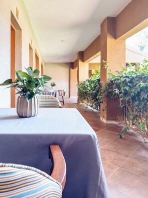 A covered outdoor dining area with a table set for two, potted plants, and a view of the surrounding greenery. - Batter Boys Boutique Hotel (Pretoria)