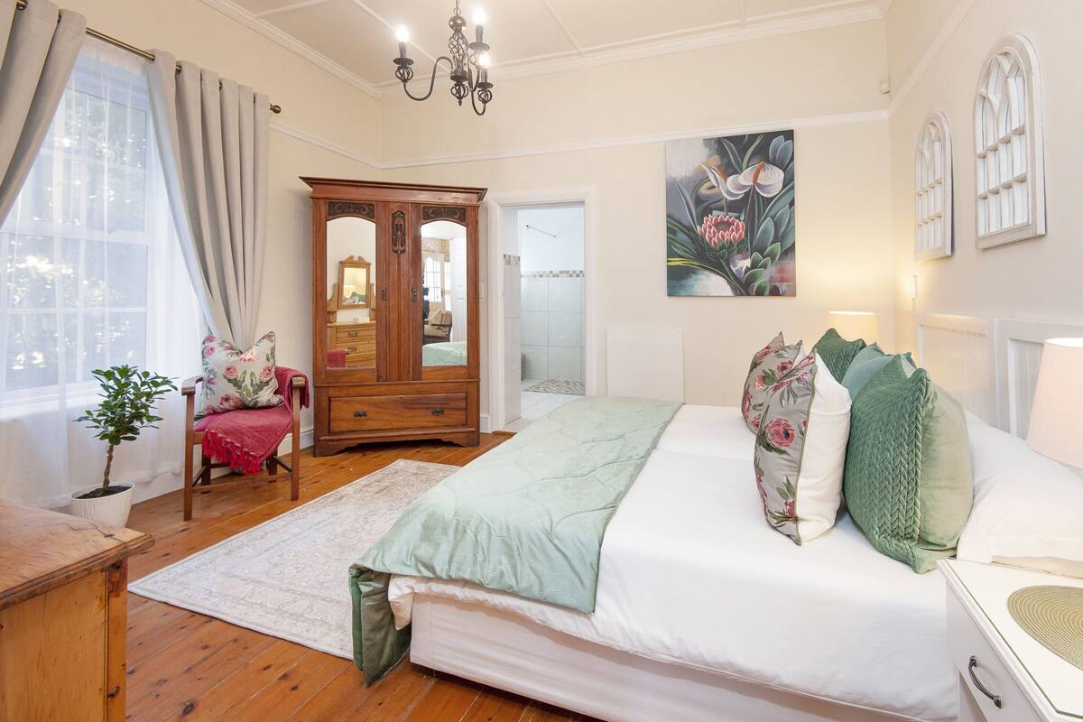 Um quarto com uma cama, um guarda-roupa de madeira, uma cadeira, uma planta em vaso e um quadro na parede.