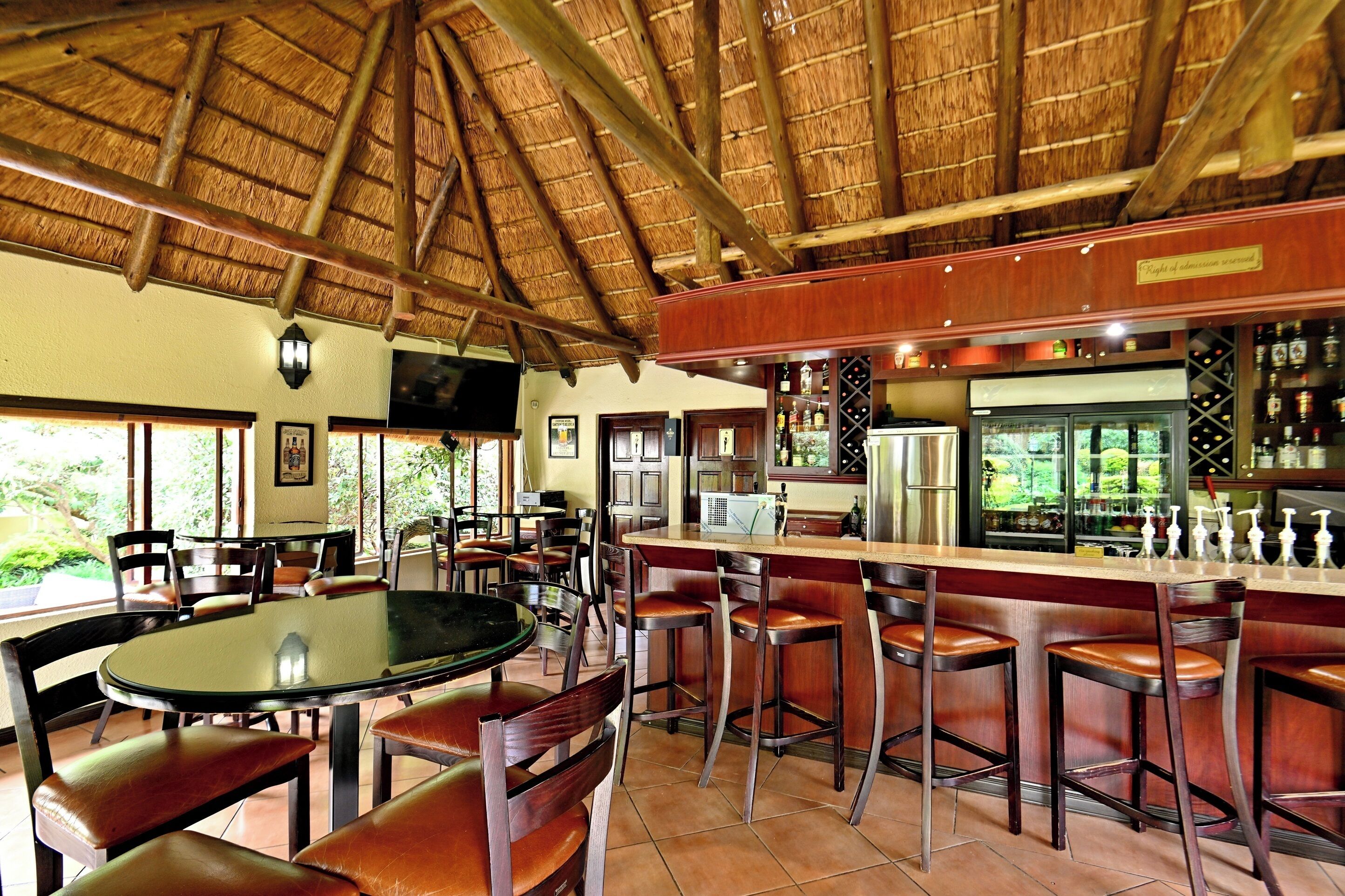 A restaurant with a thatched roof, bar area with stools, and a view of greenery outside.