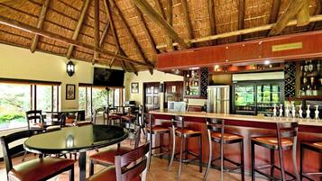 A restaurant with a thatched roof, bar area with stools, and a view of greenery outside.
