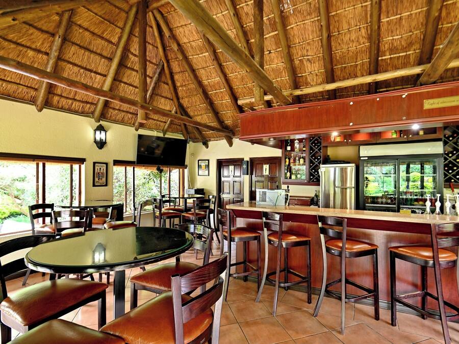 A restaurant with a thatched roof, bar area with stools, and a view of greenery outside.