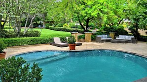 Uma piscina cercada por móveis de exterior e vegetação.