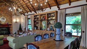 Uma sala de estar ampla com uma mesa de jantar de madeira, assentos confortáveis, lareira e uma grande janela com vista para o verde.