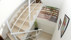 A spiral staircase with white railings and beige steps, leading to a balcony with a view of a wooden deck and palm trees. - Pousada Rosa (Penha)