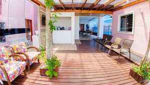 A sunlit room with a wooden floor, colorful patterned chairs, a small table, and a potted plant. - Pousada Rosa (Penha)