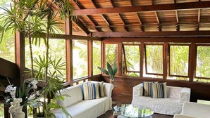 Ein geräumiger Raum mit Holzboden, hohen Decken und großen Fenstern. Mehrere weiße Sofas und ein runder Couchtisch sind vorhanden.