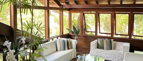 A spacious room with wooden flooring, a high ceiling, and large windows. There are several white sofas and a round coffee table.