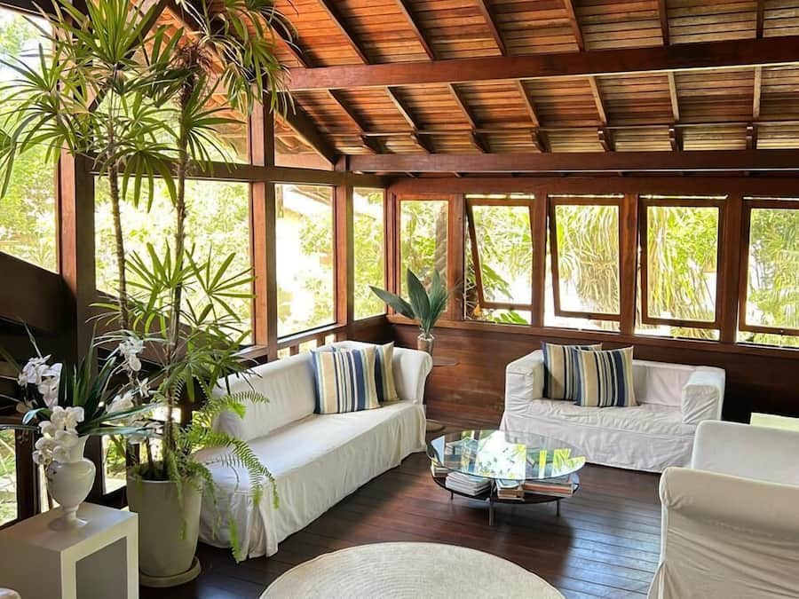 Una habitación amplia con suelo de madera, techo alto y ventanas grandes. Hay varios sofás blancos y una mesa de centro redonda.