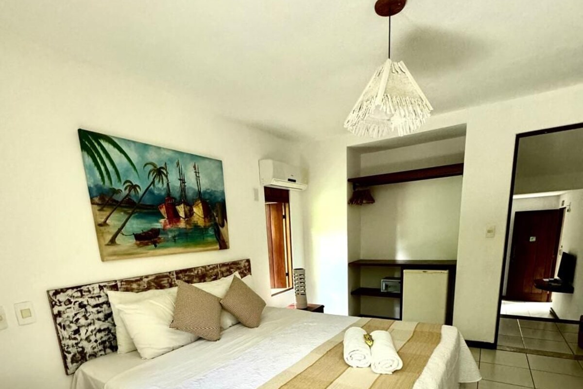 Una habitación de hotel con una cama grande, un cuadro en la pared y una kitchenette al fondo.