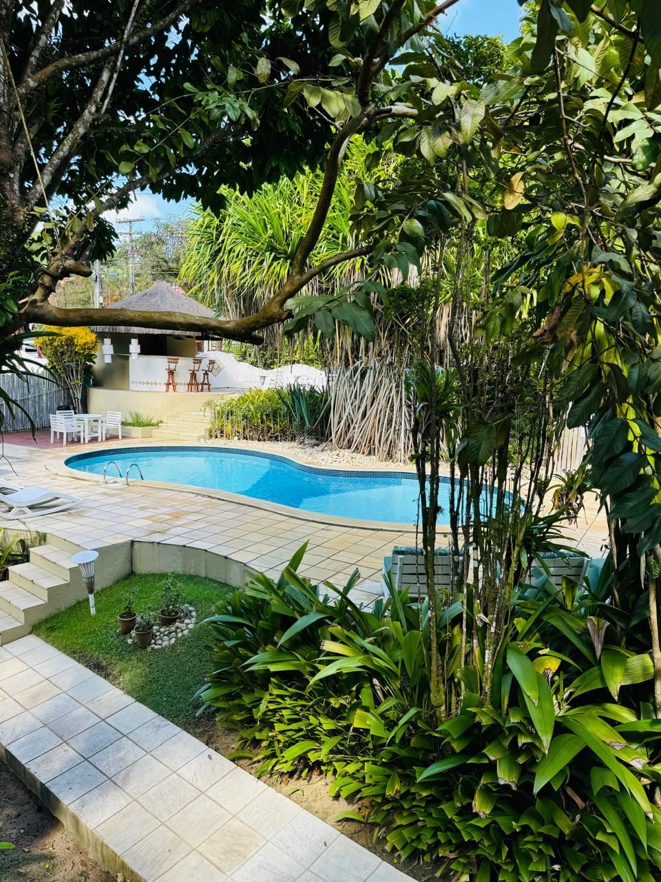 A swimming pool surrounded by a garden with various plants and a small patio area with outdoor furniture.