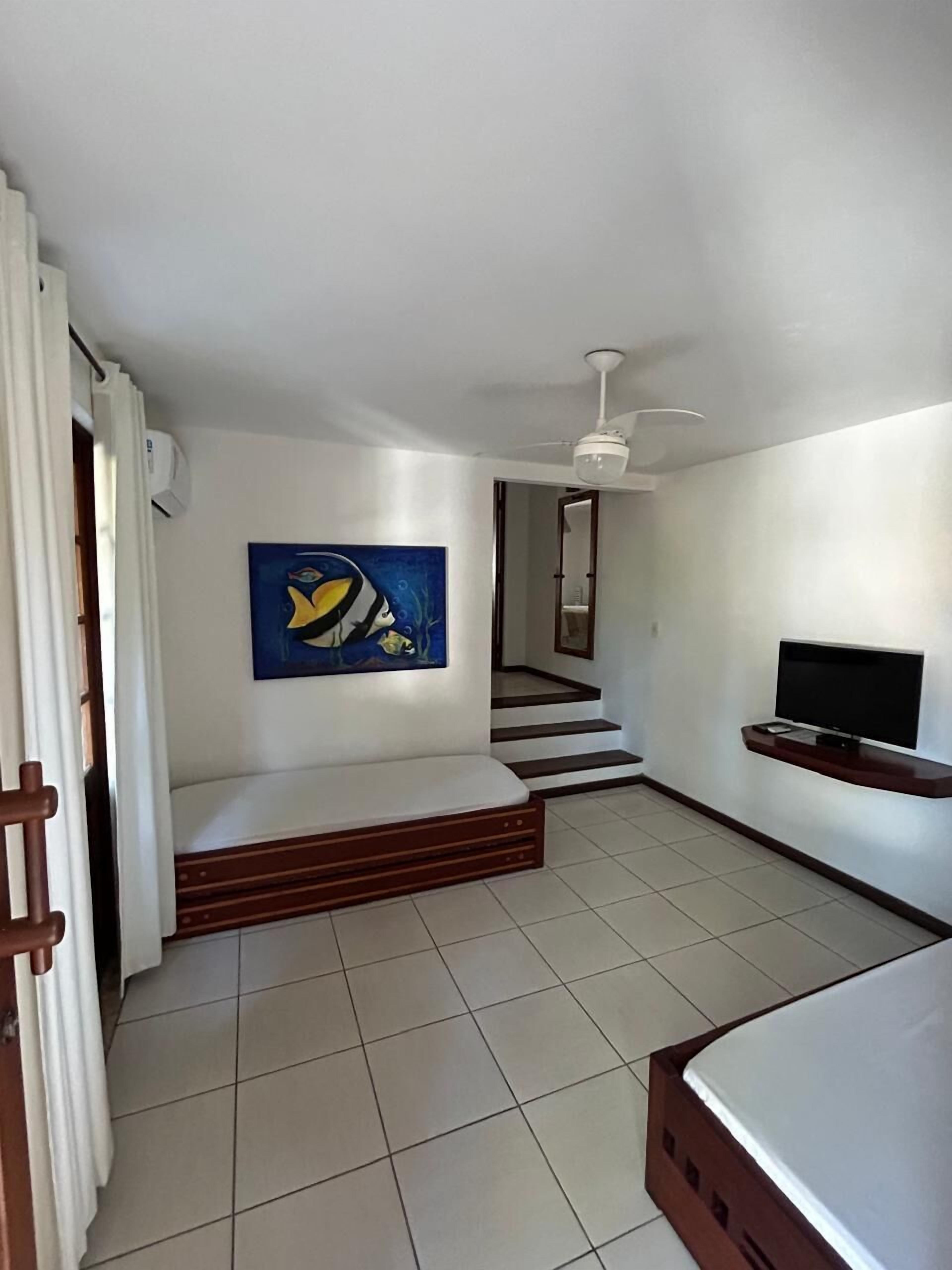 A room with a bed, a TV, a ceiling fan, a painting, and a staircase.