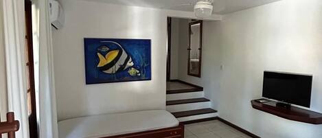 A room with a bed, a TV, a ceiling fan, a painting, and a staircase.