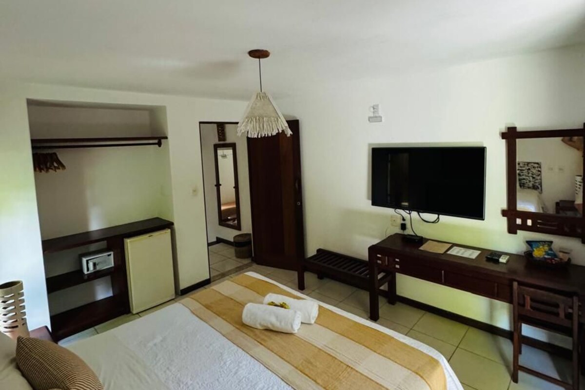 Quarto de hotel com cama, secretária, televisão, guarda-roupa e uma pequena cozinha.