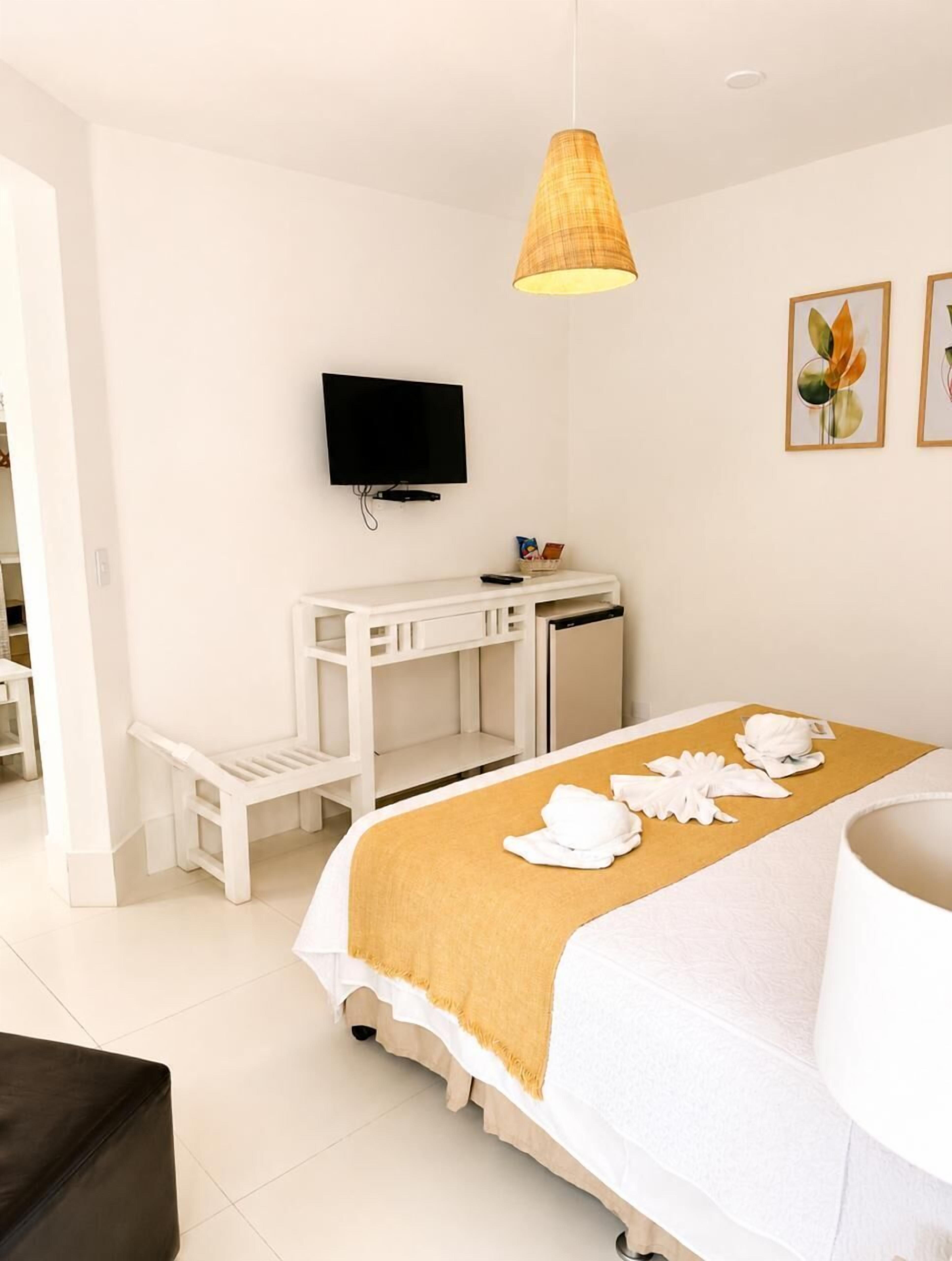 A hotel room with a bed, a desk, a television, and artwork on the wall.