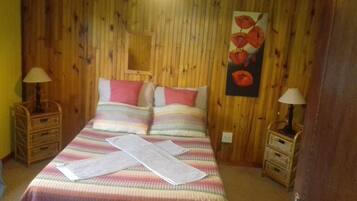 Ein Schlafzimmer mit einer holzverkleideten Wand, einem Bett mit gestreifter Bettwäsche, zwei Nachttischen mit Lampen und einem Bild von roten Blumen an der Wand.