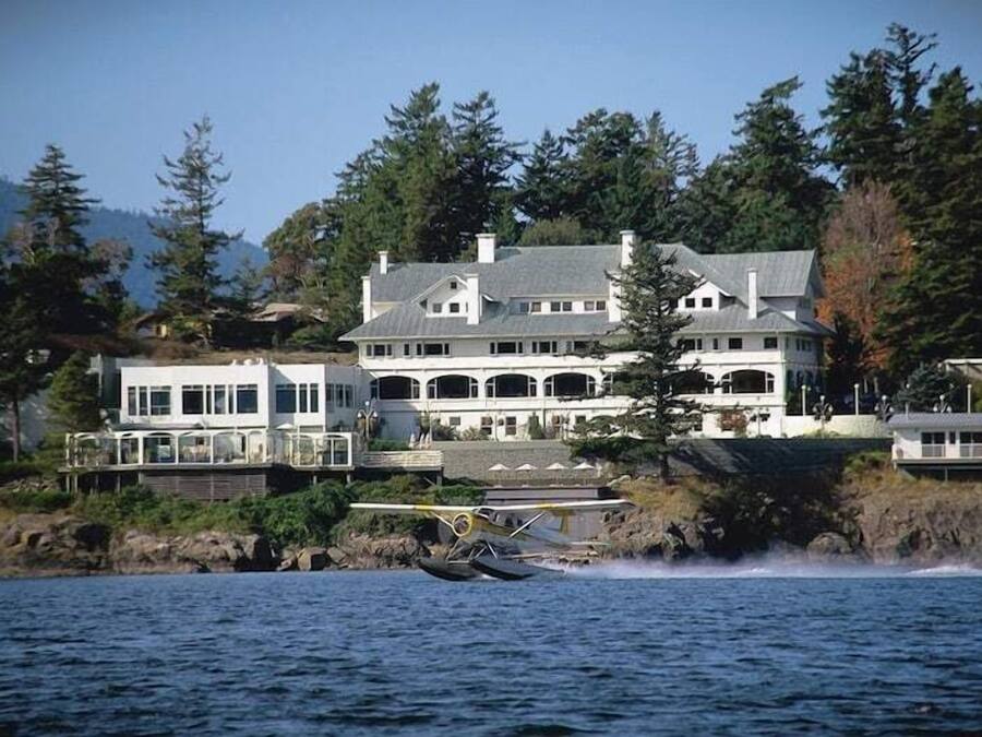 Una casa grande de varios pisos con vista al agua, un muelle y un hidroavión.