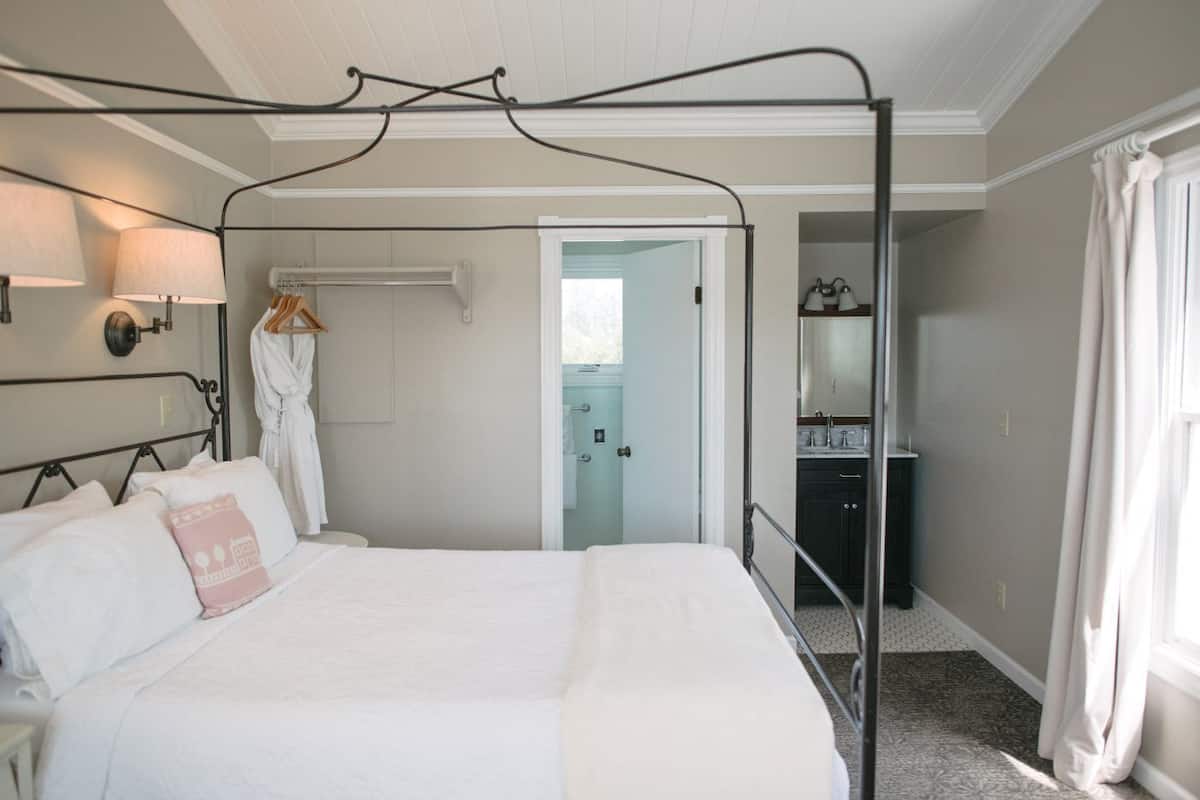 A bedroom with a four-poster bed, a walk-in closet, and a bathroom visible through an open door.