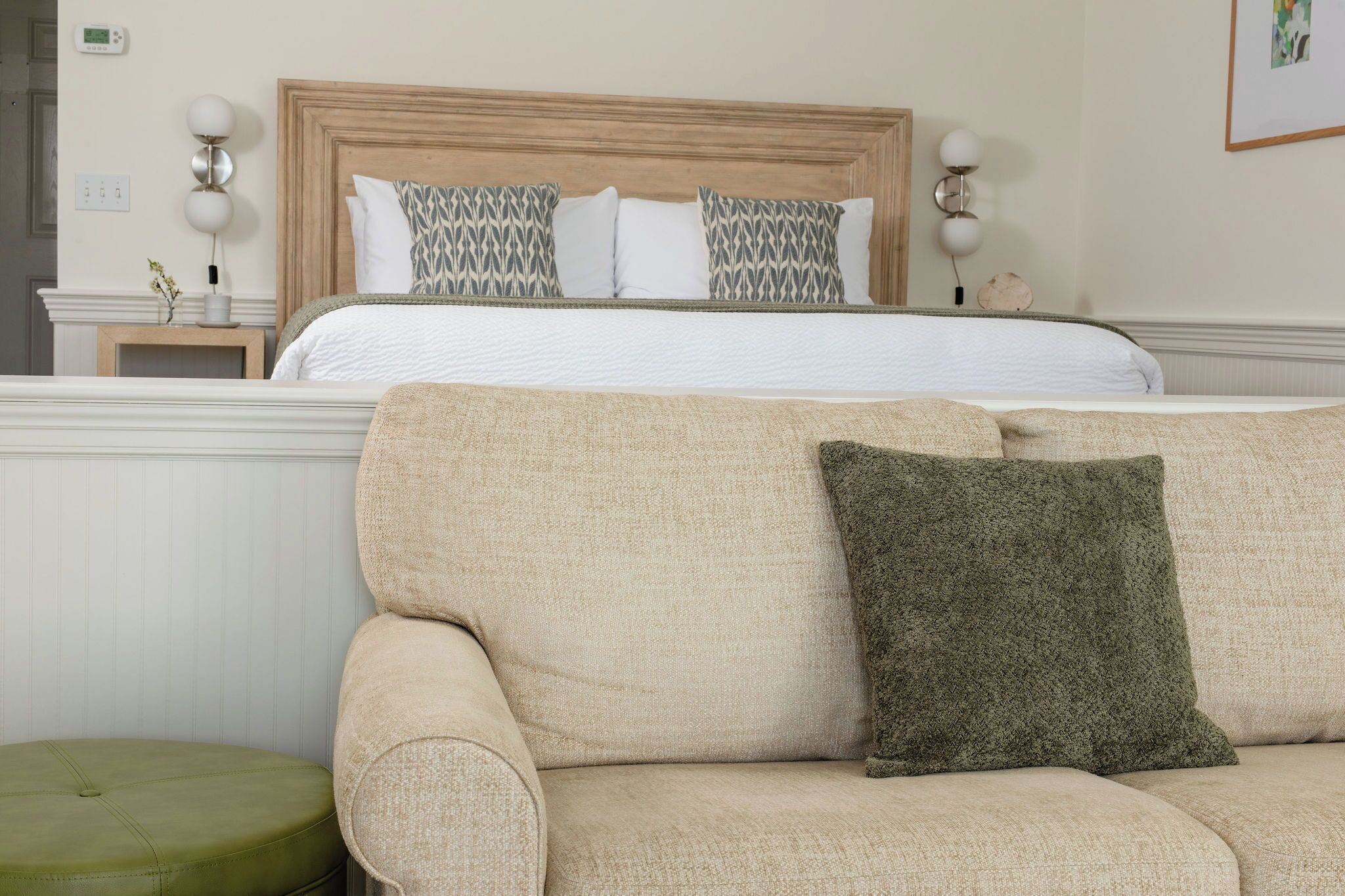 A hotel room with a bed, a beige sofa, and a green ottoman.