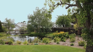 A residential garden with a pond, various plants, and a wooden bridge.
