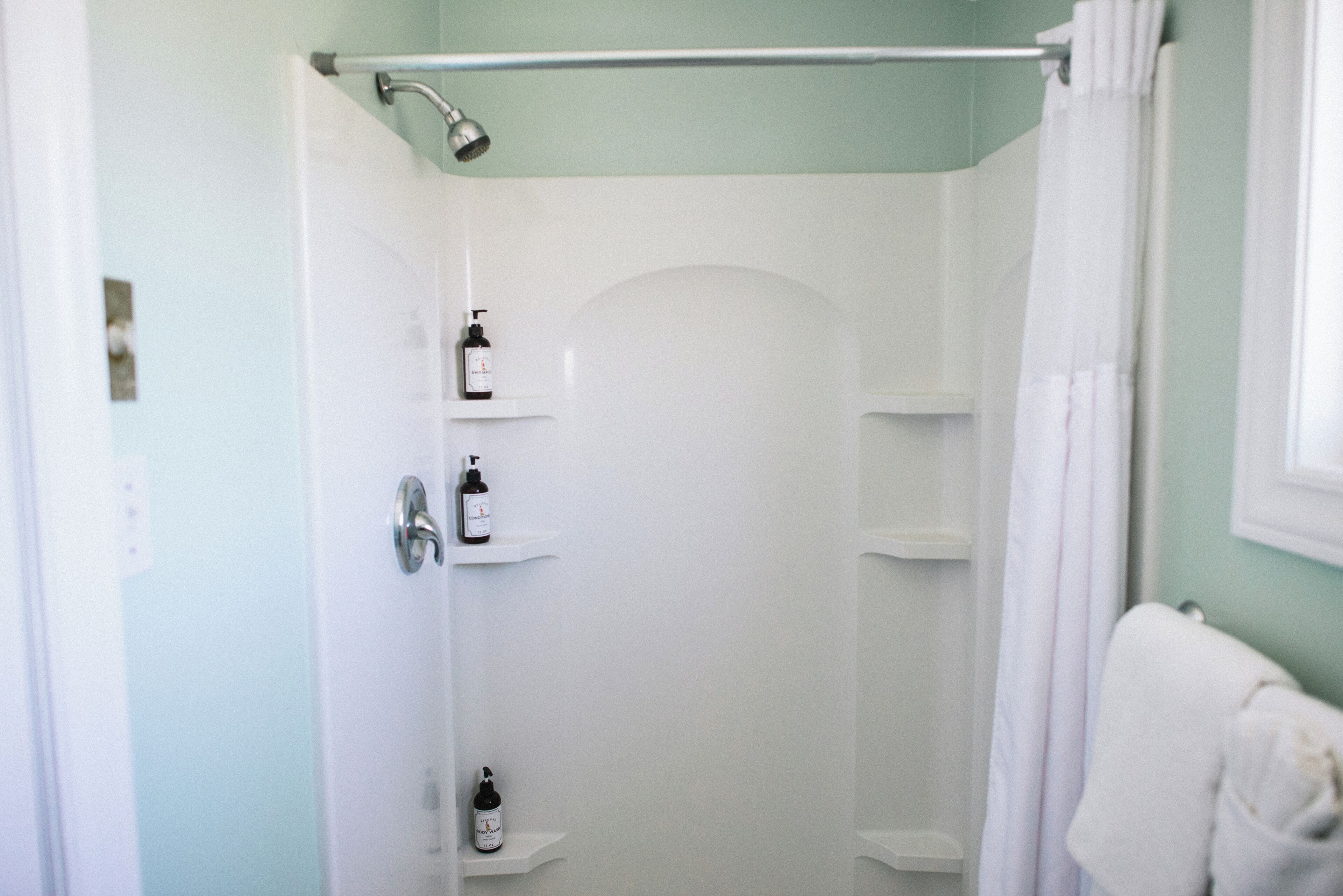 Eine Dusche mit Duschbrause, ein weißes Handtuch und zwei Ablagen mit Pflegeprodukten.