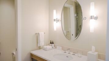 Un baño de hotel con un espejo ovalado grande, un lavamanos blanco, un perchero y dos apliques de luz.