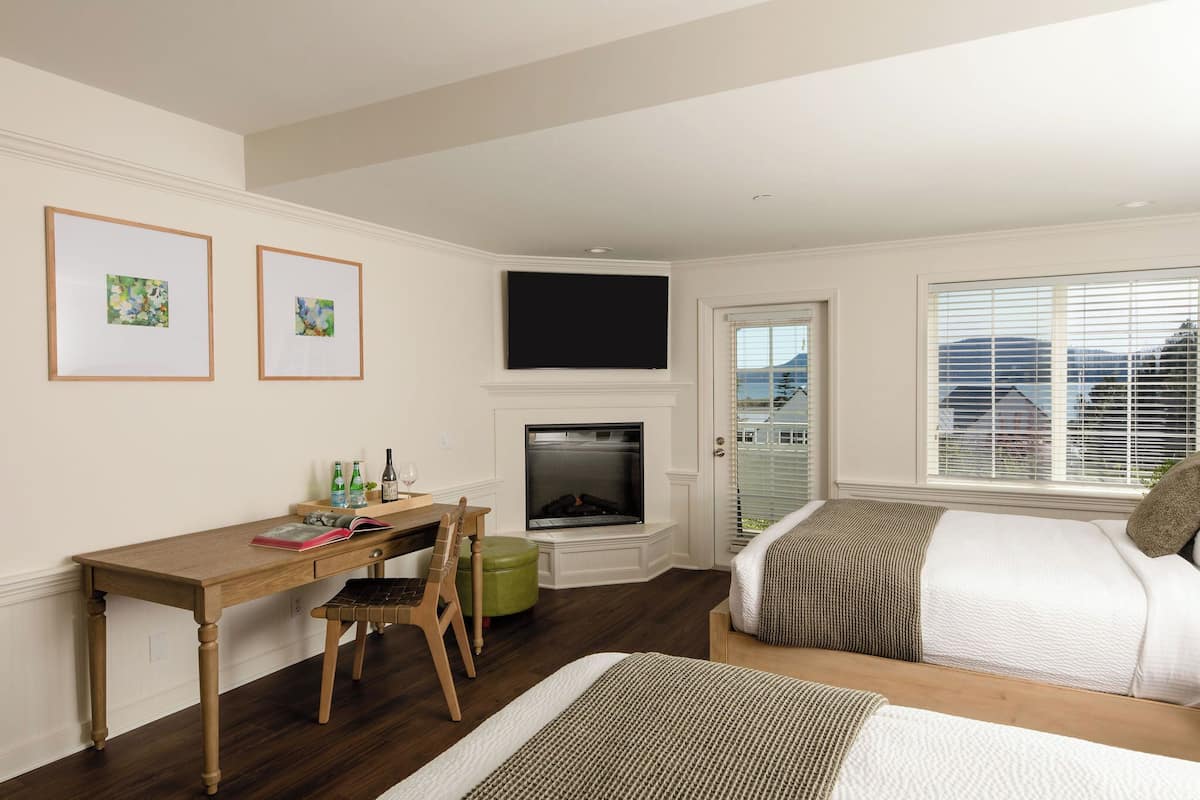 A bedroom with a desk, two beds, a fireplace, and a TV.