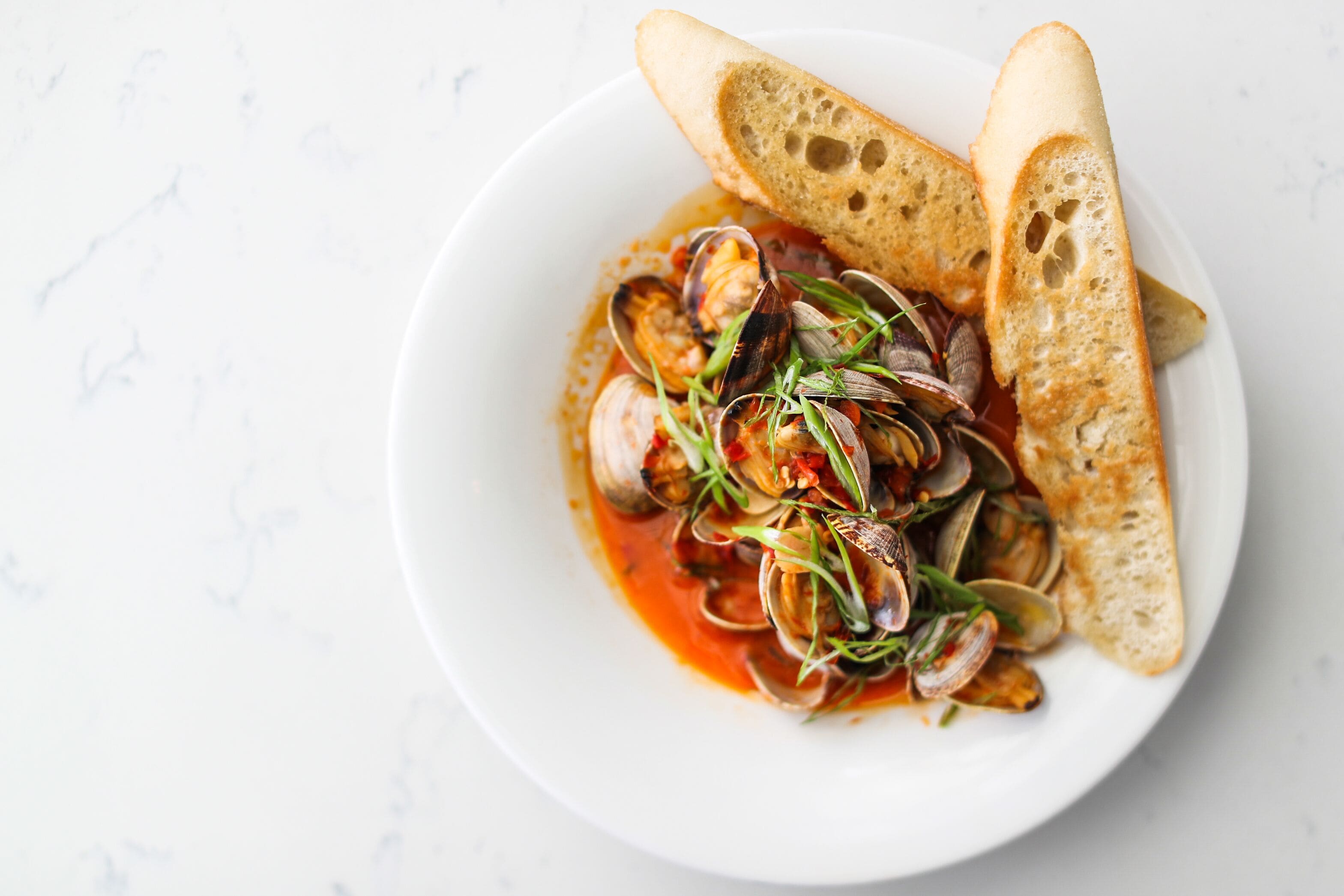 A bowl of seafood stew with clams and bread on a white plate.