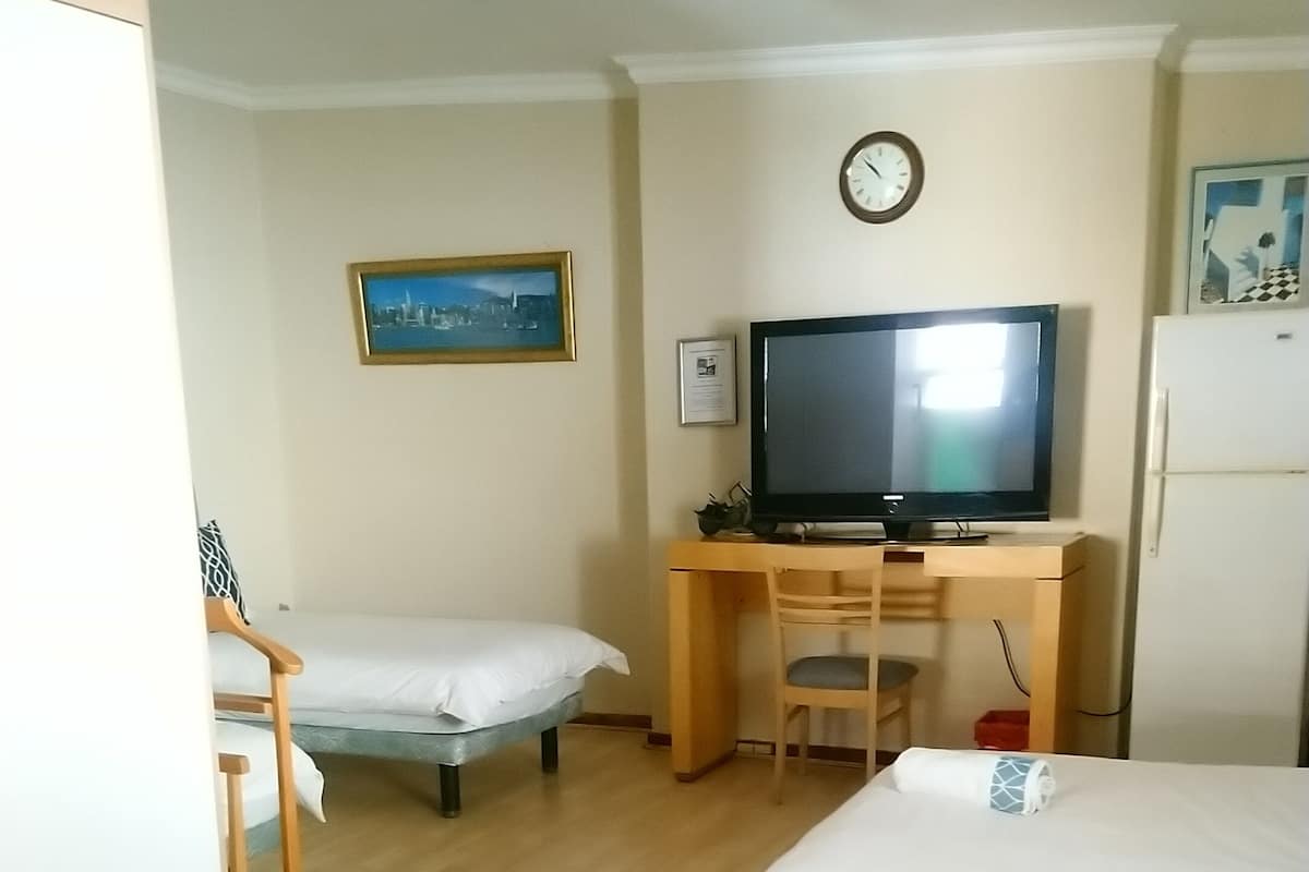 A hotel room with two single beds, a desk with a computer, a television, a clock, and a small refrigerator.