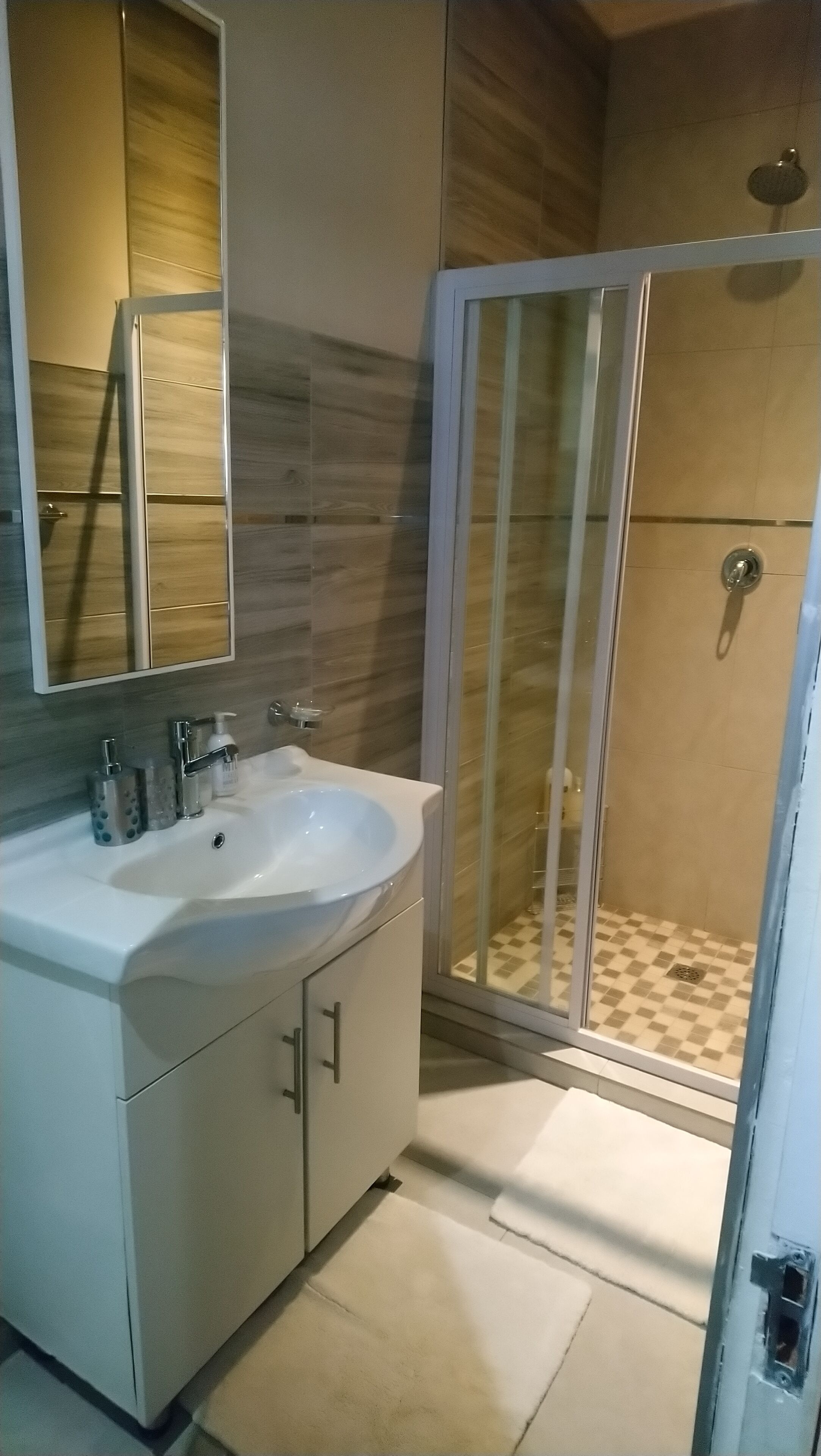 A modern bathroom with a white sink, mirror, and shower enclosure.
