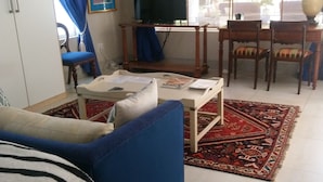 Ein Wohnzimmer mit blauem Sofa, Couchtisch, Fernseher und Essbereich mit Stühlen.